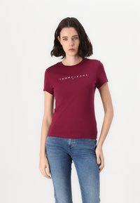 Maranjapohjainen puuvillapaita, jossa on pyöreä kaula-aukko, lyhyet hihat ja valkoinen "TOMMY JEANS" -logo rinnassa. Yksinkertainen istuva muotoilu.