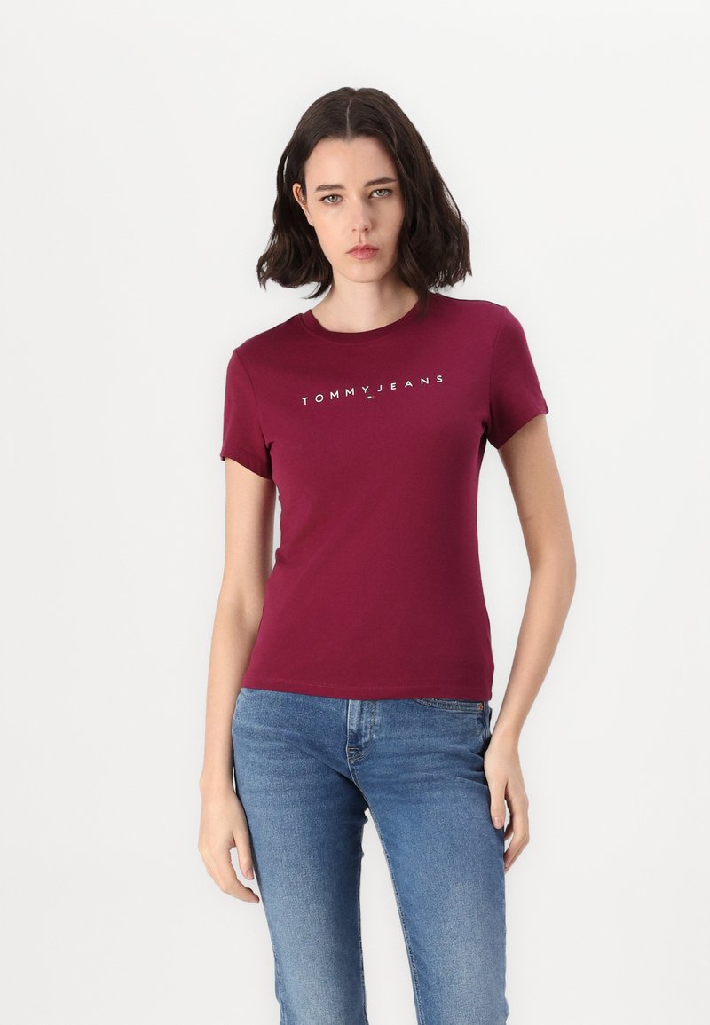 Maranjapohjainen puuvillapaita, jossa on pyöreä kaula-aukko, lyhyet hihat ja valkoinen "TOMMY JEANS" -logo rinnassa. Yksinkertainen istuva muotoilu.