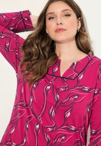 Fuchsia top met botanische print in roze en zwart. Heeft een V-vormige halslijn en lange mouwen. Zachte stof met een ontspannen pasvorm.