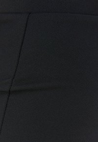 Svart tyg med en slät textur, som har ett subtilt mönster och rena sömmar. Materialet verkar stretchigt och figurnära.