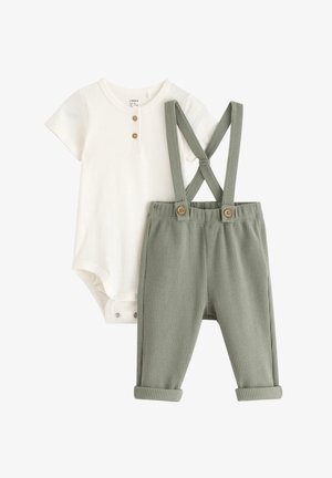 Valkoinen lyhyttoppinen bodysuit, jossa on nappiaksentteja, yhdistettynä vihreisiin tekstuuri-housuihin, joissa on suspensiot ja puunapit vyötäröllä.