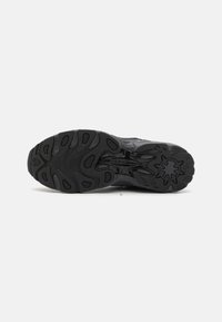 Suola di sneaker atletiche nere con scanalature profonde, gomma texturizzata e un dettaglio centrale del logo. Presenta più modelli di grip per una migliore aderenza.