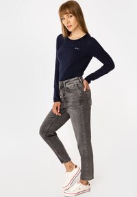 Granatowa bluzka z długim rękawem, szare jeansy z wysokim stanem oraz białe trampki. Strój charakteryzuje się dopasowanym krojem, gładką fakturą i subtelnym logo.