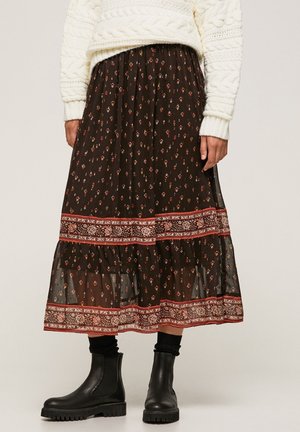 Kvinde iført sort midi nederdel med blomsterprint og røde mønstrede bånd, kombineret med sorte ankelstøvler og en hvid kabelstrikket sweater.