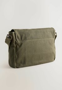 Olivgrüne Canvas-Umhängetasche mit großem Deckel, verstellbarem Tragegurt und einer hinteren Reißverschluss-Tasche; zeichnet sich durch eine glatte, strukturierte Oberfläche aus.