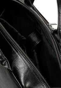 Černá kožená kabelka se zipem, s hladkým vnějším povrchem a texturovanou podšívkou uvnitř. Viditelná vnitřní kapsa.