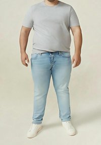 Vaqueros de mezclilla azul claro con acabado desteñido, combinados con una camiseta ajustada de algodón gris y zapatillas blancas. Diseño casual y sencillo.