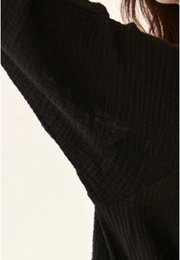 Top nero, con texture e vestibilità ampia. Presenta un design stropicciato, maniche larghe e un collo a V sottile. Materiale morbido e leggero.