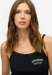 Zwarte geribde tanktop met kantafwerking, met een knoopsluiting aan de voorkant en witte tekst "SUPERDRY BOSTON" op de borst. Eenvoudig en nauwsluitend ontwerp.