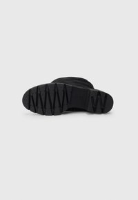 Schwarze Knöchelstiefeletten mit einer strukturierten Gummisohle, die ein Zickzackmuster für besseren Halt aufweist, und einem weichen Stoff-Obermaterial, das für Komfort und Langlebigkeit entwickelt wurde.