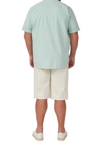 Helles grünes kurzärmliges Hemd, beiger Shorts, weiße Sneakers. Lässige Passform mit einem Rückenfalte am Hemd und knielangen Shorts.
