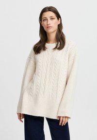 Pull en laine crème avec motif en maille torsadée, offrant une coupe décontractée, des poignets larges en côtes et un motif texturé sur l'ensemble. Matière douce et pelucheuse.