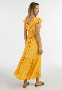 Rochie maxi galbenă cu mâneci volă, talie ajustată și tiv în mai multe niveluri. Țesătură fină cu un design de spate în V. Purtați-o cu sandale plat.