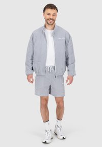 Stripet lett jakke og shorts sett i blått og hvitt, laget av mykt stoff, med elastisk midje og glidelås foran.