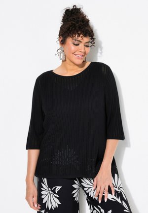 Schwarzes, geripptes Strickoberteil mit runden Ausschnitt und Dreiviertelärmeln, kombiniert mit gemusterten Hosen mit großen Blumenakzenten.