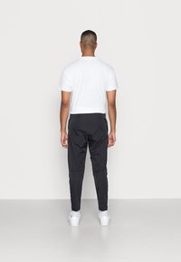 Black athletic pants with a tapered design, paired with a white short-sleeve t-shirt. White sneakers complete the outfit.