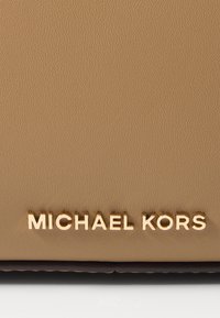 Produit en cuir tan avec une surface texturée ; présente un logo doré en relief "MICHAEL KORS" en bas.