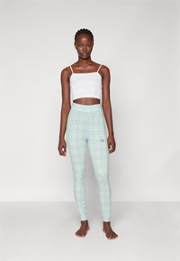 White cropped tank top and light blue patterned leggings with diamond shapes and green accents, featuring an embroidered logo on the side.