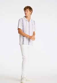 Camisa de manga corta en blanco con rayas verticales azules y patrones geométricos. Combinada con pantalones blancos y zapatos de color claro.