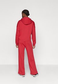 Červená mikina s kapucňou a šnúrkou v páse, spolu so zodpovedajúcimi nohavicami s širokými nohavicami, vyrobená z mäkkého materiálu. Má pohodlný strih a detaily so švami.