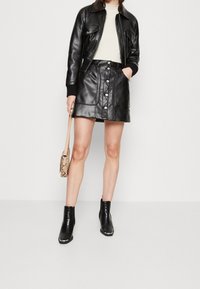 Svart bomberjacka i läder, krämfärgad topp, svart läderminikjol med knappar framtill och svarta ankelstövlar med krokodilmönster.