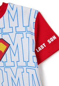 Camiseta infantil con esquema de colores blanco y rojo, presenta texto azul y un emblema amarillo y rojo. La impresión notable dice "ÚLTIMO HIJO."