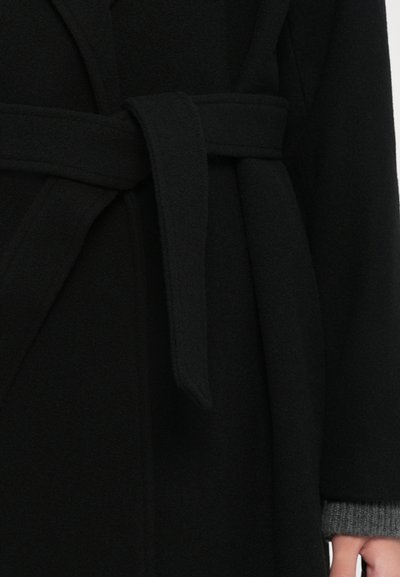 Black wool coat tied at the waist with a belt, showing part of the sleeve and hand wearing a gray knit cuff underneath.