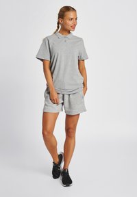 Grau Poloshirt und passende Shorts aus weichem Baumwollmix. Mit einem klassischen Kragen, kurzen Ärmeln und seitlichen Taschen. Getragen mit schwarzen Sneakern.
