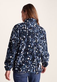 Fleece pullover with a high collar, featuring a blue, white, and black abstract pattern, long sleeves, and a relaxed fit.