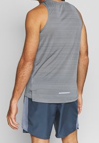 Gray athletic tank top with a textured pattern, paired with dark blue shorts featuring light gray accents. Back view shows sleeveless design.