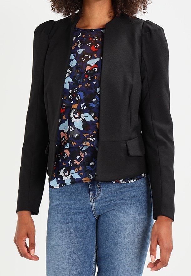 Blazer noir cintré avec épaulettes, présentant une coupe ajustée et des poches frontales, porté sur un chemisier fleuri. Jean en denim visible en dessous.