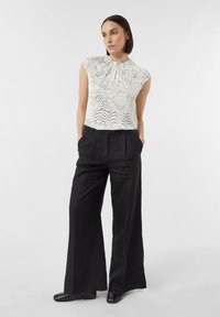 White blouse with black speckles, round neckline, and ruffled detail, paired with wide-leg black trousers made of a textured fabric.