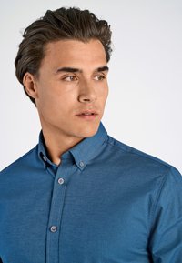 Sinisestä, pehmeästä kankaasta valmistettu nappipaita, jossa on sileä pinta, klassinen kaulus ja neljä kontrastiväristä nappia.