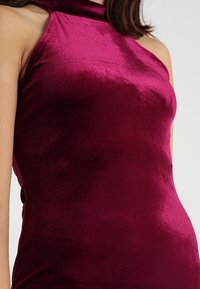 Haut bustier en velours bordeaux avec une texture lisse, une coupe ajustée et des épaules découvertes, mettant en valeur un éclat subtil et un drapé doux.