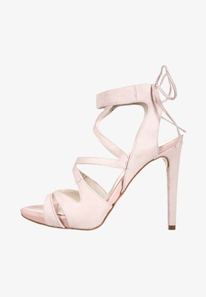 Sandal de tacón alto de ante rosa con tiras entrecruzadas, un lazo en el tobillo y una punta brillante. El tacón de aguja añade altura.