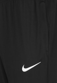 Schwarze Sporthosen mit glatter Textur, die ein weißes Nike-Logo auf der linken Seite und seitliche Taschen für zusätzlichen Komfort haben.