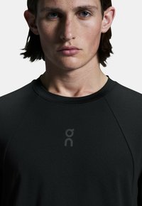 Must mustriko must shirt, ümar kaelus, raglan varrukad ja õrn hall logo rinnal. Sile tekstuur, kätkeb disain.