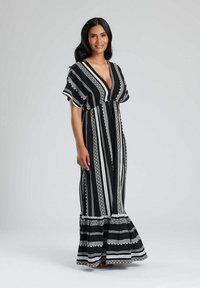 Abito maxi a righe bianche e nere con scollatura a V profonda, maniche corte e orlo arricciato. Presenta intricate fantasie tessute lungo le righe.