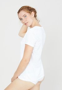 Witte katoenen T-shirt met korte mouwen, ronde halslijn en een ontspannen pasvorm, weergegeven vanuit een zijaanzicht tegen een effen achtergrond.