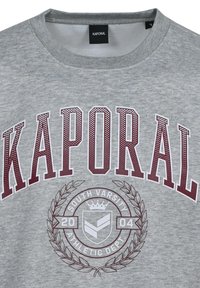 Sudadera gris con la inscripción "KAPORAL" en grandes letras color burdeos, un logo atlético circular con diseño de laurel y un cuello de tripulación acanalado.