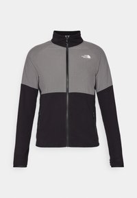 Giacca in fleece grigia e nera della North Face con zip completa, colletto alto e tasche laterali con zip, caratterizzata da un sottile motivo a rete nella parte superiore.