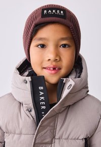 Dunjakke i lysegrå med høj krave, med sort inderside. Brun ribstrikket hue med et sort mærke med teksten "BAKER".