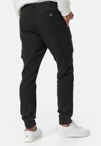 Sort cargo-bukser med elastiske manchetter og sidelommer, med knaplukning og et tekstureret stof. Kombinationen med hvide sneakers.