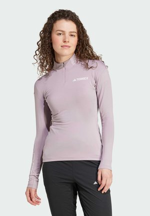 Haut de sport à manches longues, couleur violet clair, avec un col zippé. Il comporte un logo TERREX sur la poitrine et des panneaux latéraux texturés pour la respirabilité.