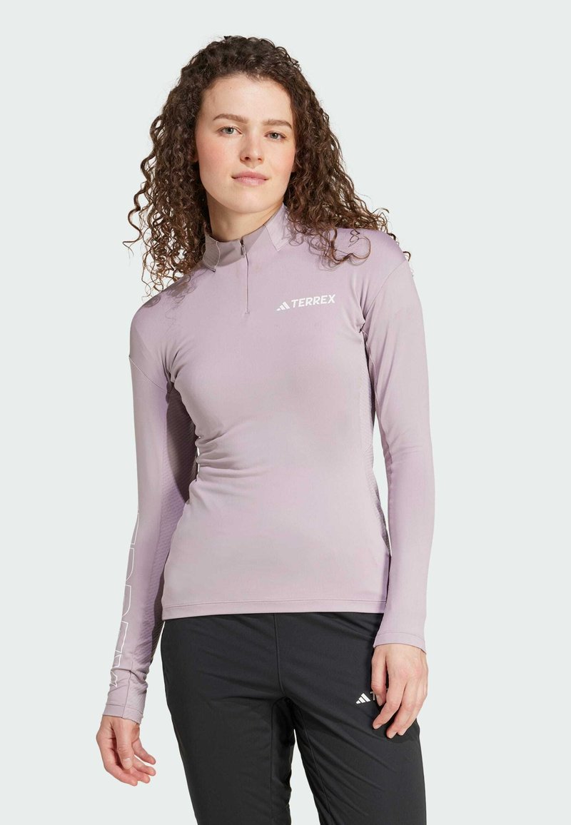 Maglietta atletica a maniche lunghe di colore viola chiaro con colletto con zip. Presenta un logo TERREX sul petto e pannelli laterali texturizzati per una maggiore traspirabilità.