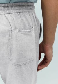 Light grey linen pants with an elastic waistband, featuring a back pocket and smooth texture. Side view shows the pocket design clearly.