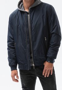 Marinblå bomberjacka med en grå huva, framdragkedja, sidofickor och ribbad mudd, tillverkad av ett glansigt, slätt tyg.