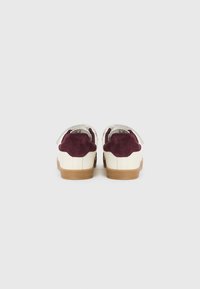 Leather sneakers with a white body, maroon suede heel accents, and a textured gum sole. Features flat laces and a round toe design.