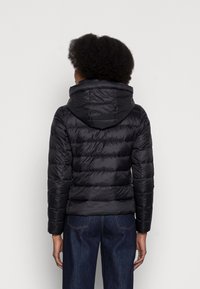 Czarna kurtka puchowa z kapturem, z pikowanym wzorem i elastycznymi mankietami. Noszona z ciemnymi dżinsami. Gładki, błyszczący materiał.