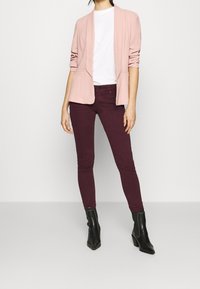 Světle růžový blazer s ohrnutými rukávy, bílým tričkem, krémově červenými skinny džíny a černými vysokými kotníkovými botami. Jednoduchý design s přiléhavým střihem.